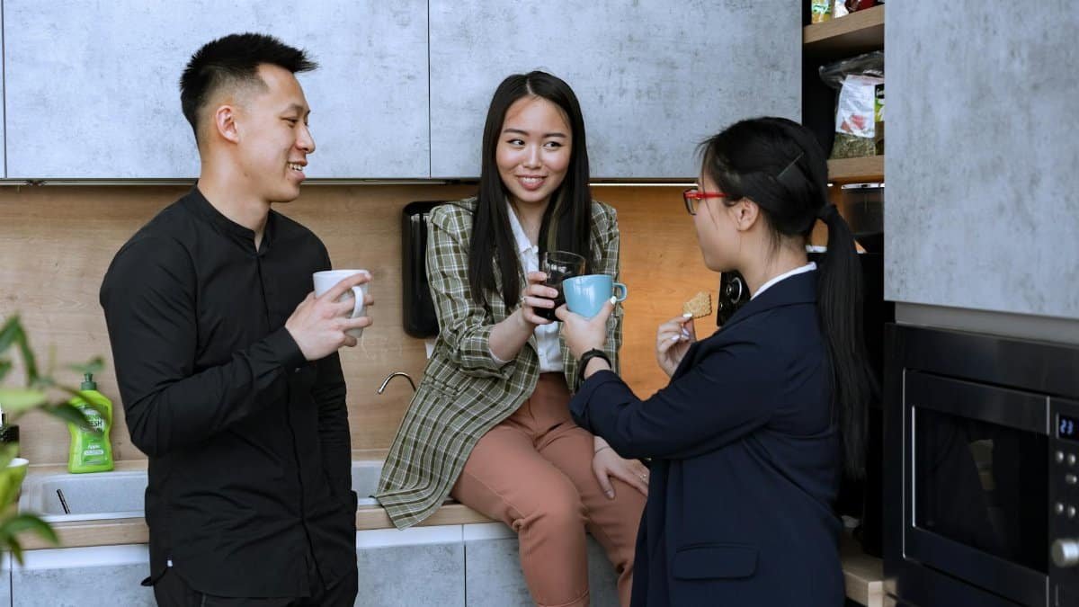 Office colleagues enjoy a coffee break in the kitchen, engaging in friendly conversation.