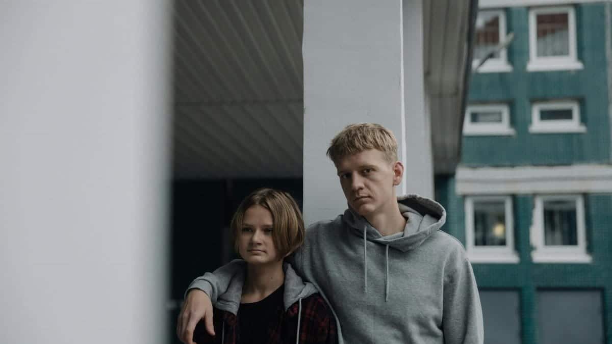Two siblings in casual wear leaning against a pillar, showcasing a relaxed urban vibe.