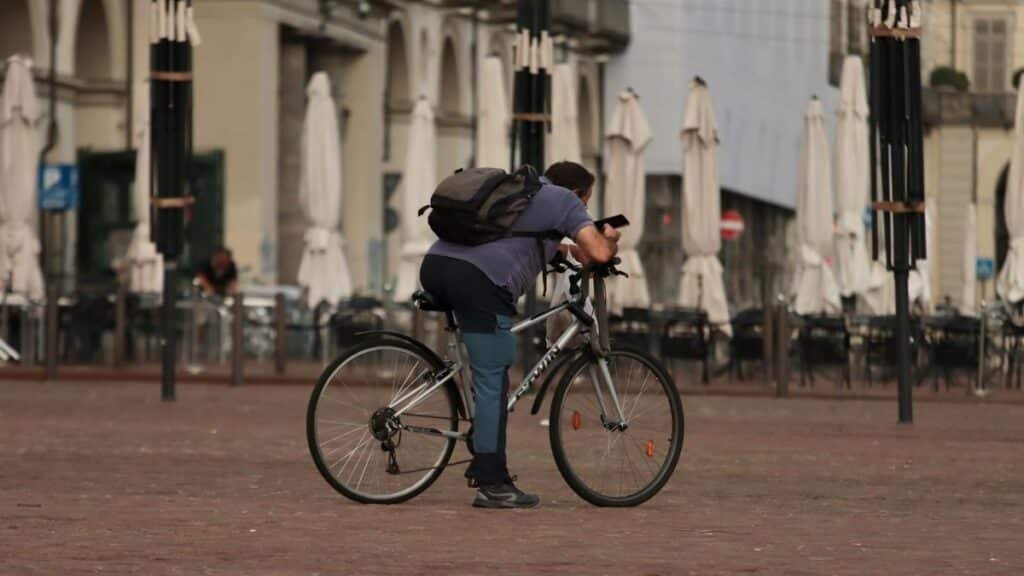 A man takes a break on his bicycle in a quiet town square, leaning over the handlebars.