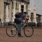 A man takes a break on his bicycle in a quiet town square, leaning over the handlebars.