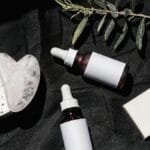 Flat lay of skincare products with gua sha and leaves on black textile. Ideal for beauty and wellness visuals.