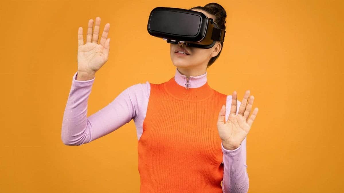 A young woman wearing VR goggles explores digital space against a yellow background indoors.