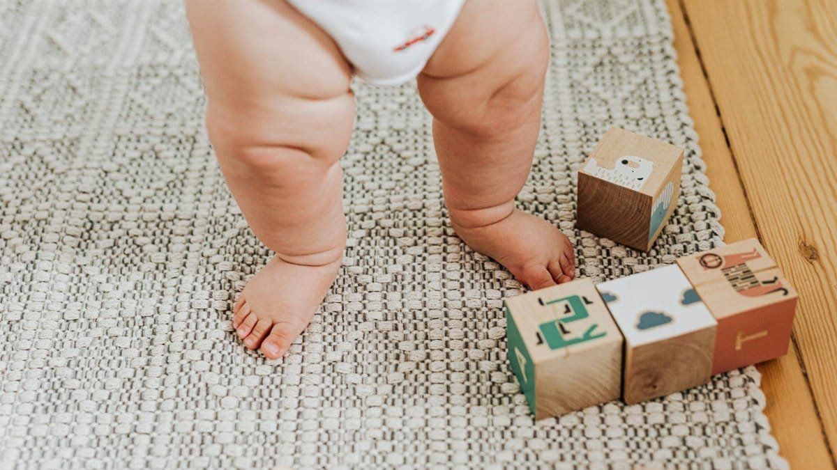 Capturing a baby's first steps with wooden building blocks on a soft indoor rug. Perfect for childhood memories.
