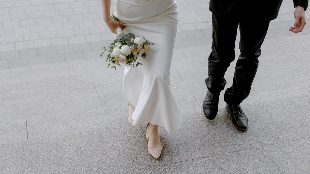 Bride and groom walking up the steps holding a bouquet and dressed elegantly.