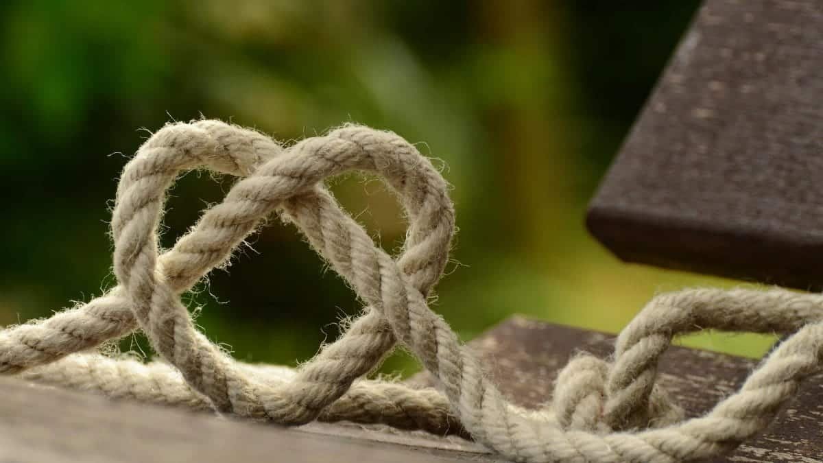 Close-up of twine forming a heart shape on a rustic wooden table outdoors.