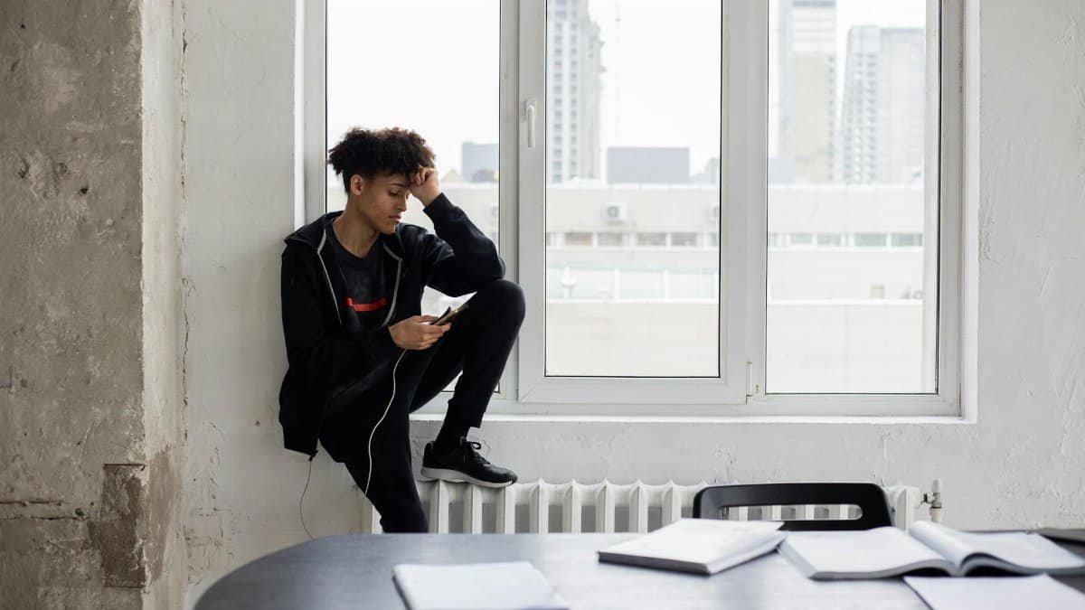 Tired African American male student surfing charging mobile phone during break in studies in loft style room