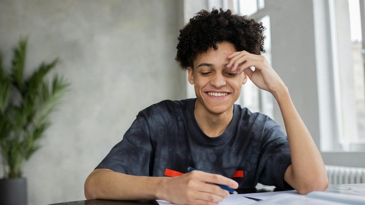 Cheerful student taking notes and studying indoors with natural lighting.