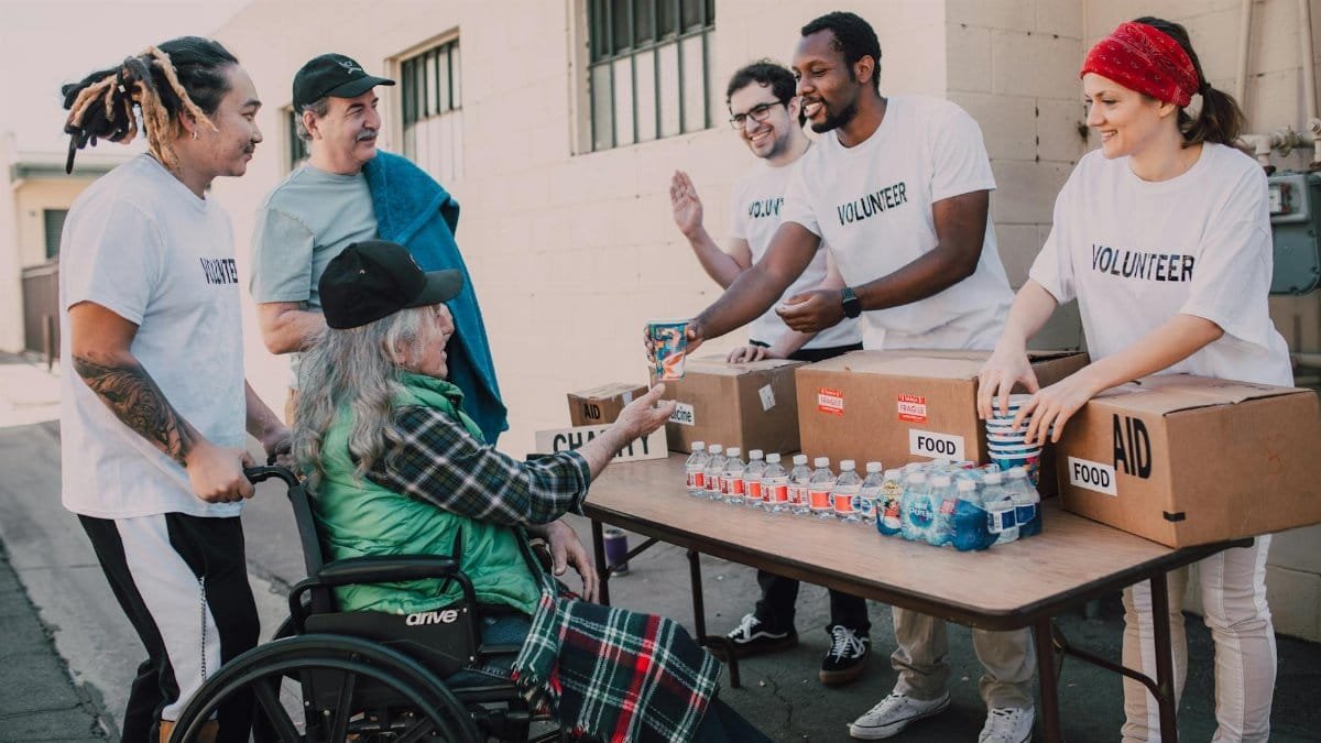 Volunteers distribute bottled water and supplies to diverse individuals in an outdoor setting, showcasing community support.