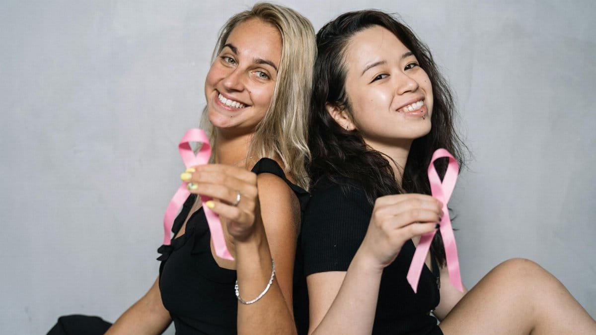Two women holding pink ribbons to promote breast cancer awareness and support.