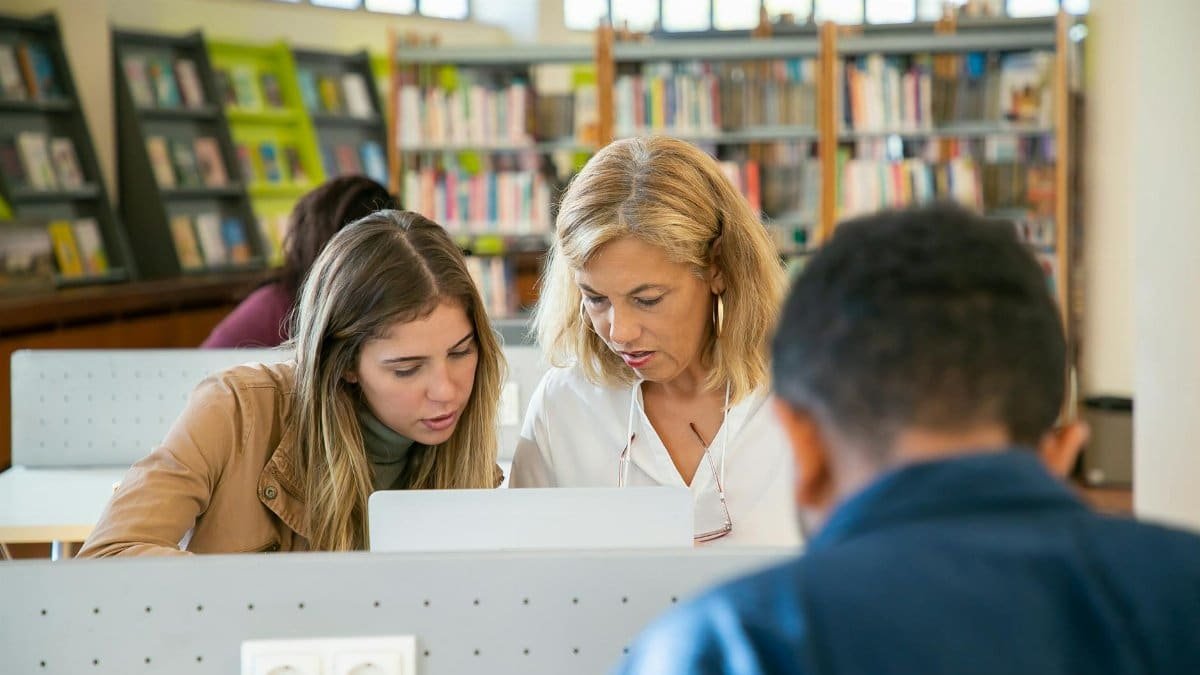 Two women focusing on laptop research in a university library.