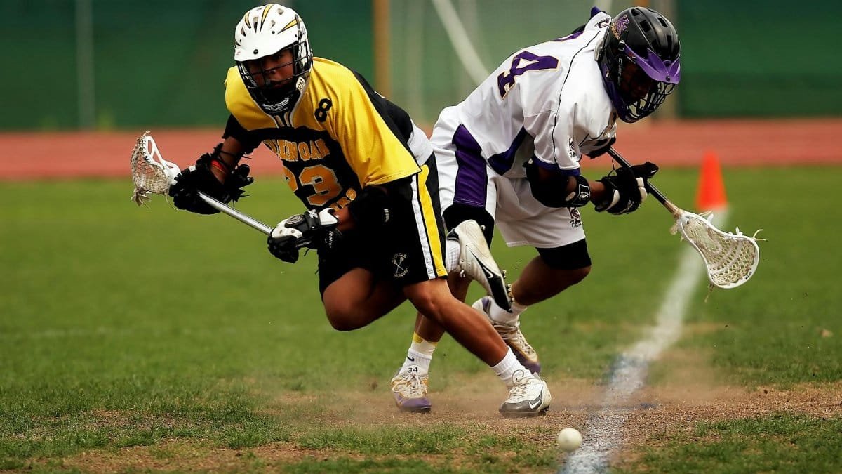 Two men playing an intense lacrosse game outdoors on a grass field.