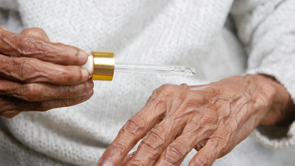 Close-up of elderly hands applying serum with dropper, focusing on skincare and aging.
