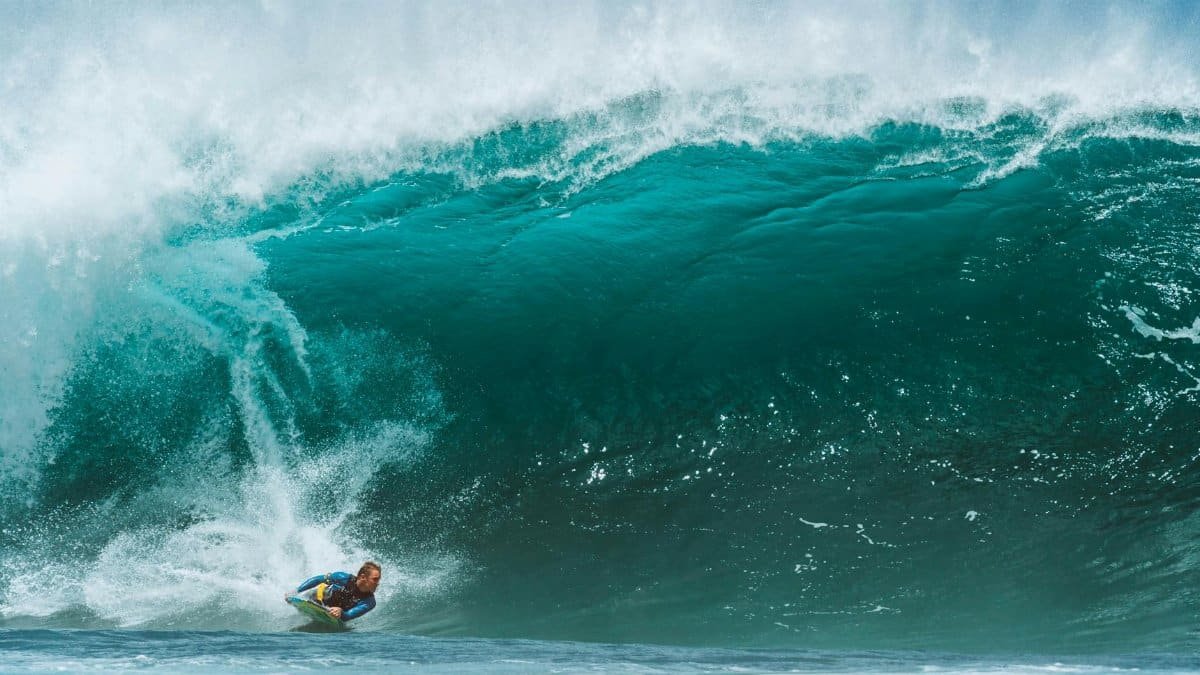 Male surfer in wetsuit surfing on foamy wave splashing in turquoise sea in tropical country