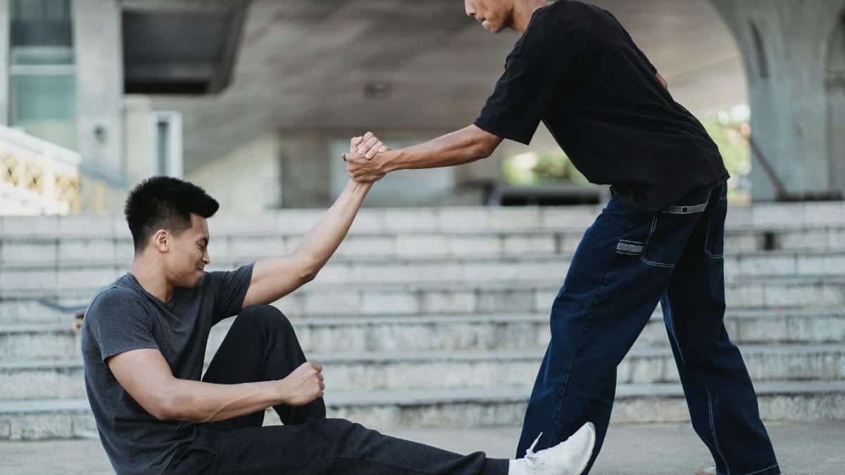 Two young men helping each other on urban city stairs, symbolizing friendship and support.