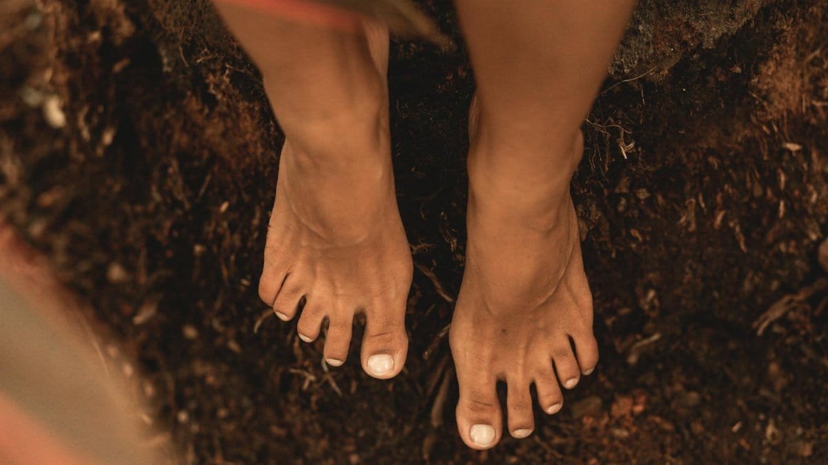Close-up of bare feet standing on earthy ground, embracing nature.