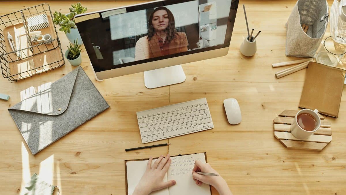Person taking notes during a video call at a neatly organized home desk, showing remote work lifestyle.