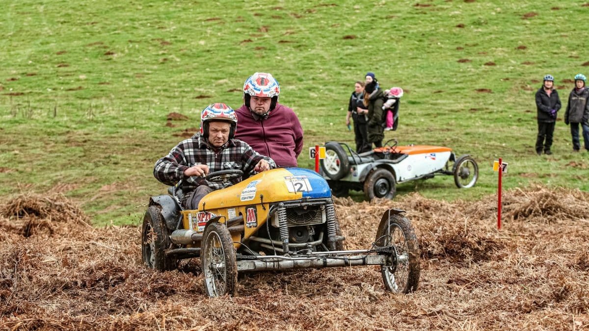 Classic sidecar motorcycles racing on grassy hills during a vintage trial event.