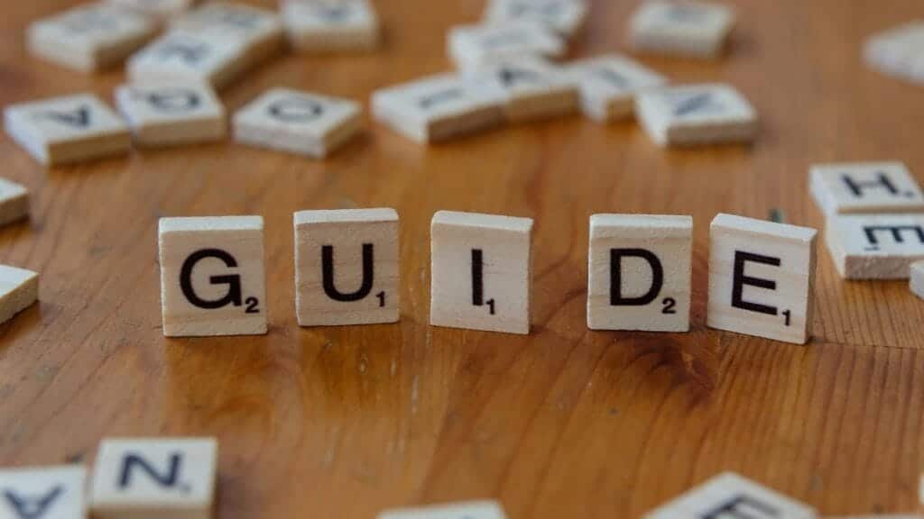 Scrabble tiles forming the word 'Guide' surrounded by scattered letters on a wooden table.