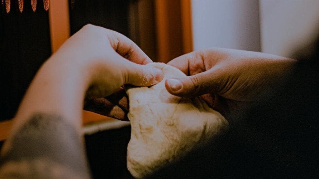 Hands kneading dough with focus on texture and technique in a warm kitchen setting.
