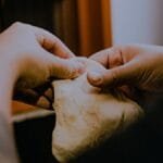 Hands kneading dough with focus on texture and technique in a warm kitchen setting.