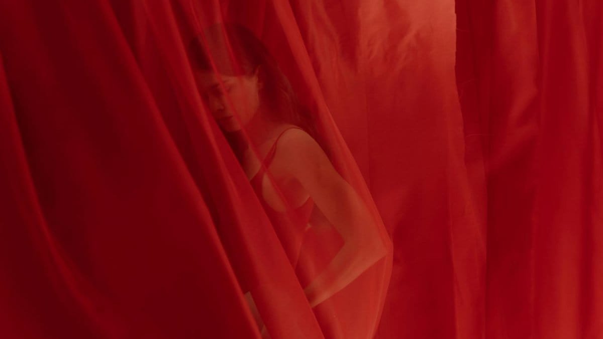 Artistic capture of a woman behind a sheer red curtain, creating a mysterious allure.