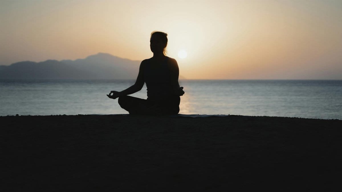 A woman practices meditation with a tranquil ocean sunset backdrop, embodying peace and relaxation.