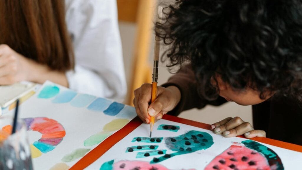 A child joyfully paints watermelon patterns, exploring creativity through art.