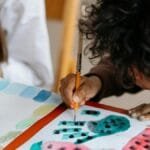 A child joyfully paints watermelon patterns, exploring creativity through art.