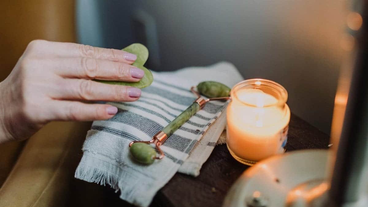 A calming self-care setup featuring a jade roller, candle, and cozy ambiance, perfect for relaxation.