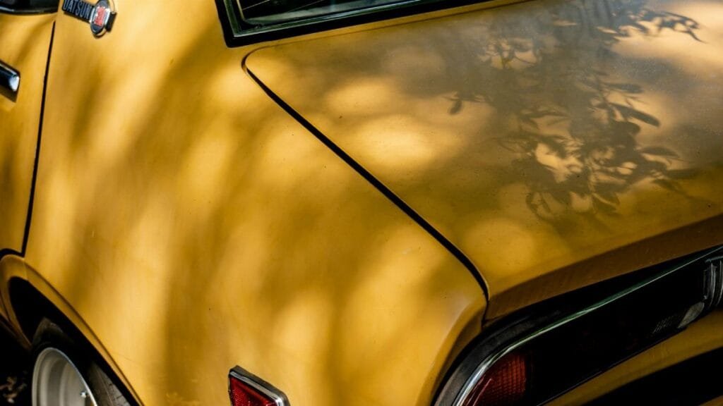 Close-up of a vintage yellow Datsun car showing tail light and shadows across the body.