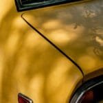 Close-up of a vintage yellow Datsun car showing tail light and shadows across the body.