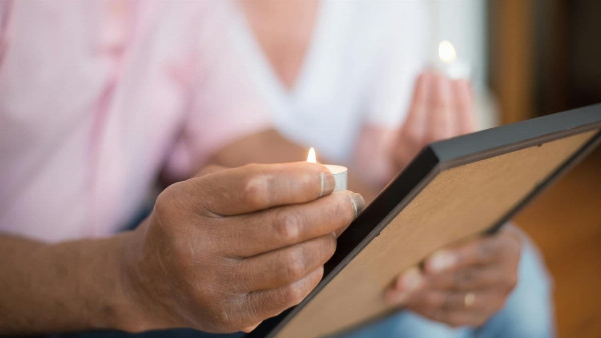 Close-up of hands holding a candle and a picture frame, symbolizing remembrance and memory.