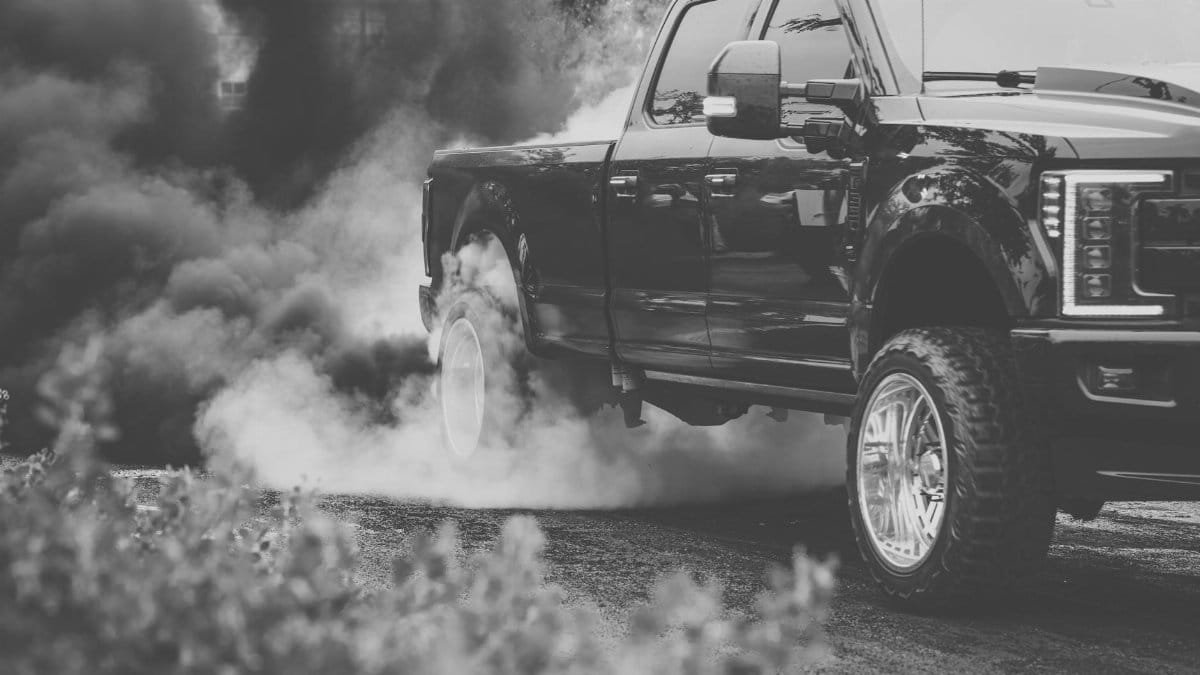Black pickup truck emitting smoke during a burnout on the road.