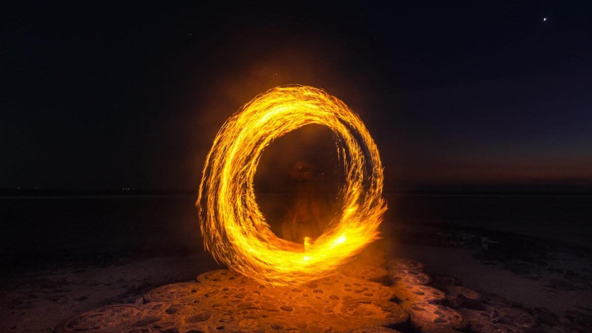 Captivating long exposure shot of a fire dancer creating fiery circles on a serene beach at night.