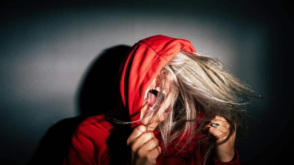 A teenager in a red hoodie screams with hair flying, conveying intense emotion.