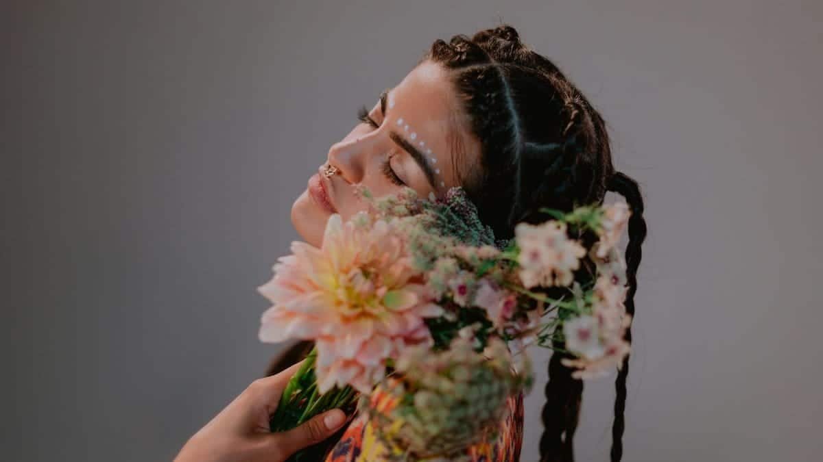 Woman with intricate braids and face paint holding a bouquet of colorful flowers, showcasing cultural beauty.