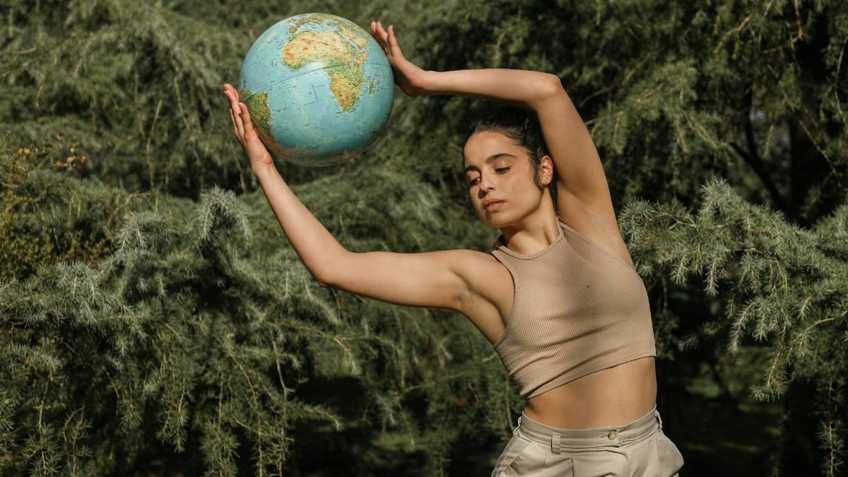 A woman gracefully poses with a globe amidst lush greenery, symbolizing environmental awareness.