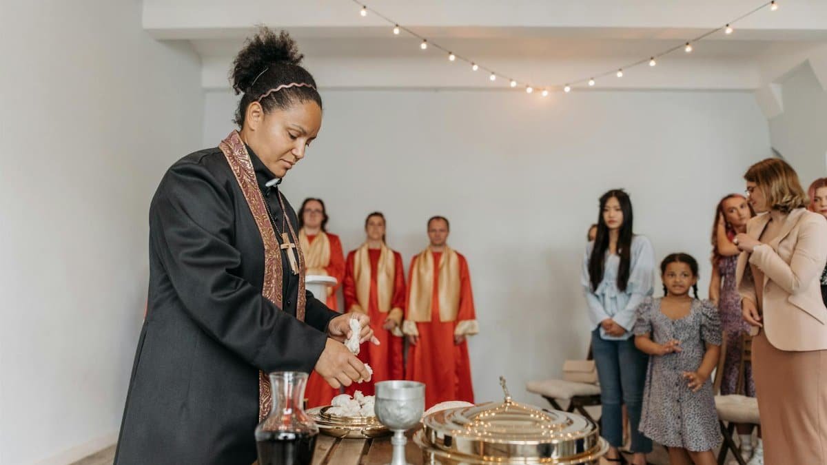 A diverse group of people attending a religious ceremony with a priest performing rituals indoors.