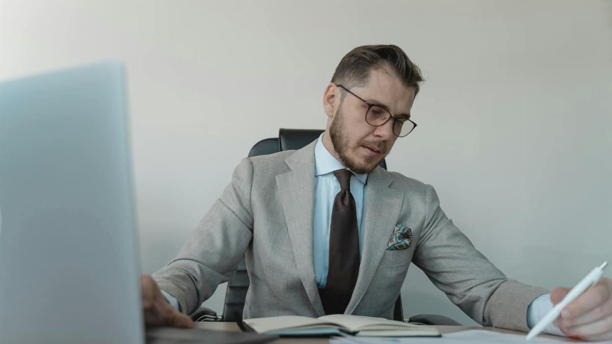 Professional businessman in gray suit working with documents and laptop in modern office.