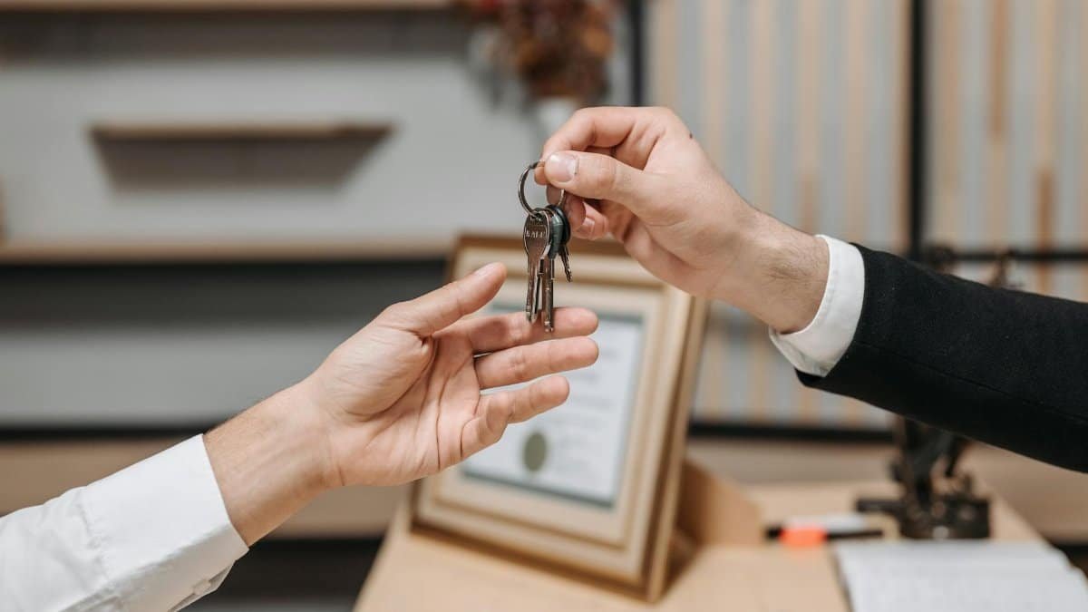 Detailed view of hands exchanging keys in a professional office environment, symbolizing real estate or business transactions.
