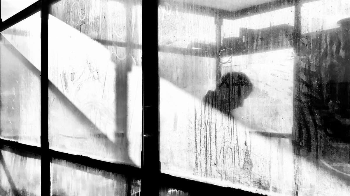 A mysterious silhouette seen through dirty fogged glass, creating an eerie black and white effect.