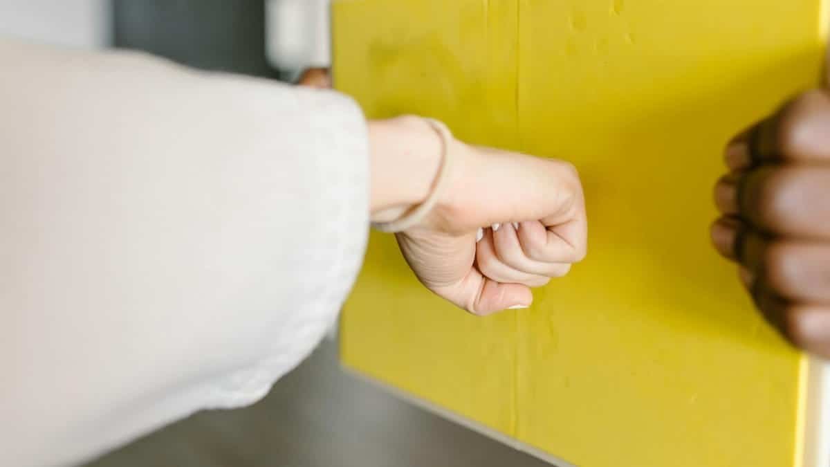 Close-up of a fist punching a yellow martial arts rebreakable board indoors.