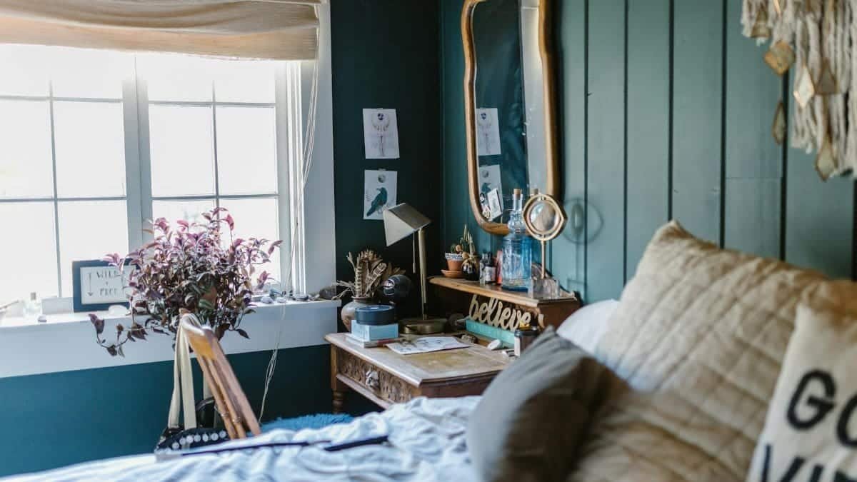 A cozy bedroom with green walls featuring crystals and a vintage mirror.