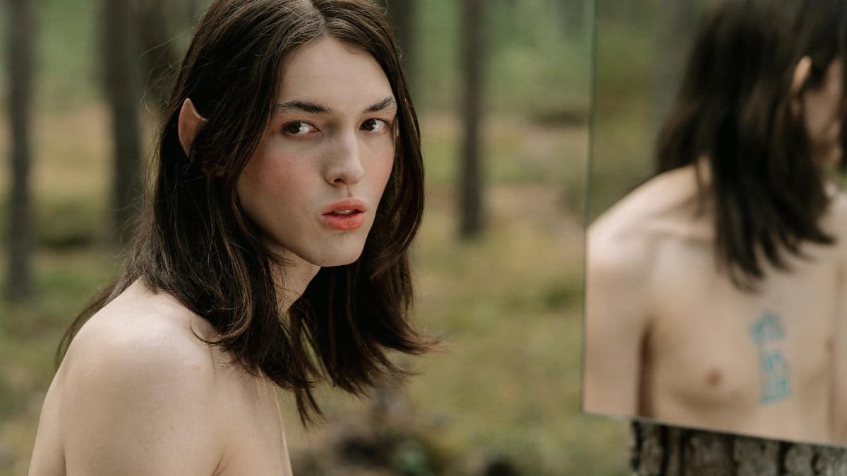 Portrait of a mystical elf character with long hair, reflecting in a forest mirror.