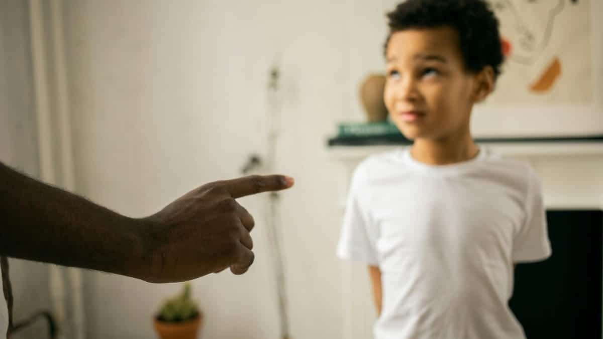 A father points and scolds his son indoors, emphasizing discipline.