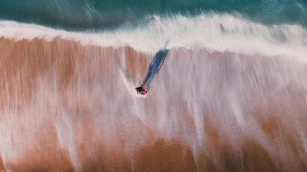 Aerial view of a solitary person walking along an empty beach, casting a long shadow.