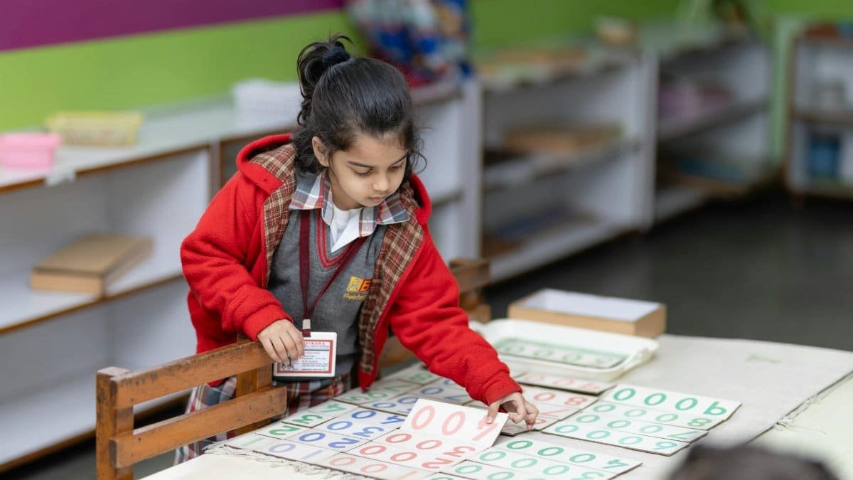 A young child in a red jacket learns numbers using educational tools in a classroom setting.