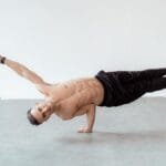 A shirtless male breakdancer in a one-handed freeze pose on a studio floor.