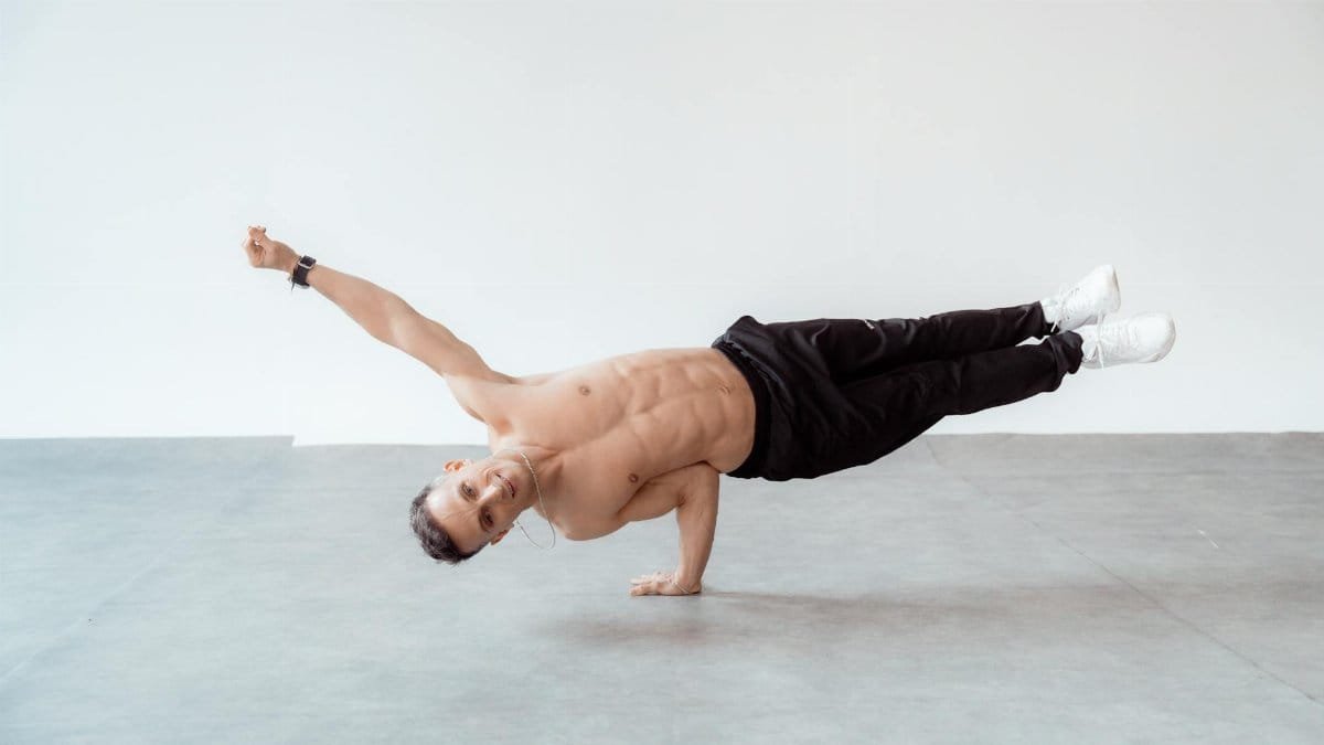 A shirtless male breakdancer in a one-handed freeze pose on a studio floor.
