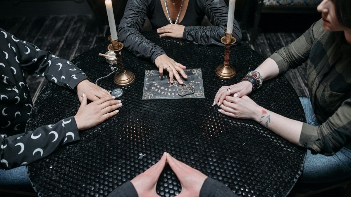 A group of adults engage in a mysterious seance using a Ouija board by candlelight.